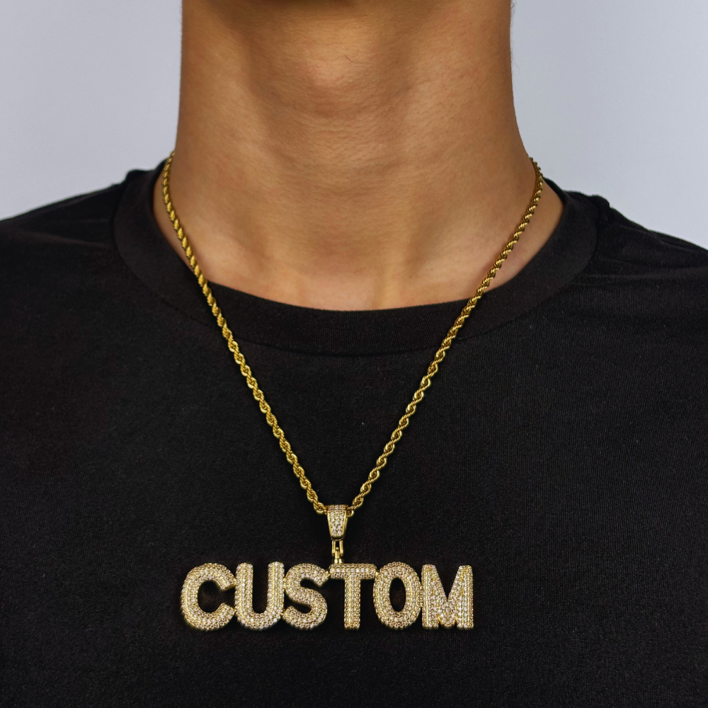 Modelo usa um pendente personalizado em dourado com zircónias cúbicas, em estilo bold e totalmente cravejado, refletindo brilho e atitude numa peça de joalharia de destaque.
