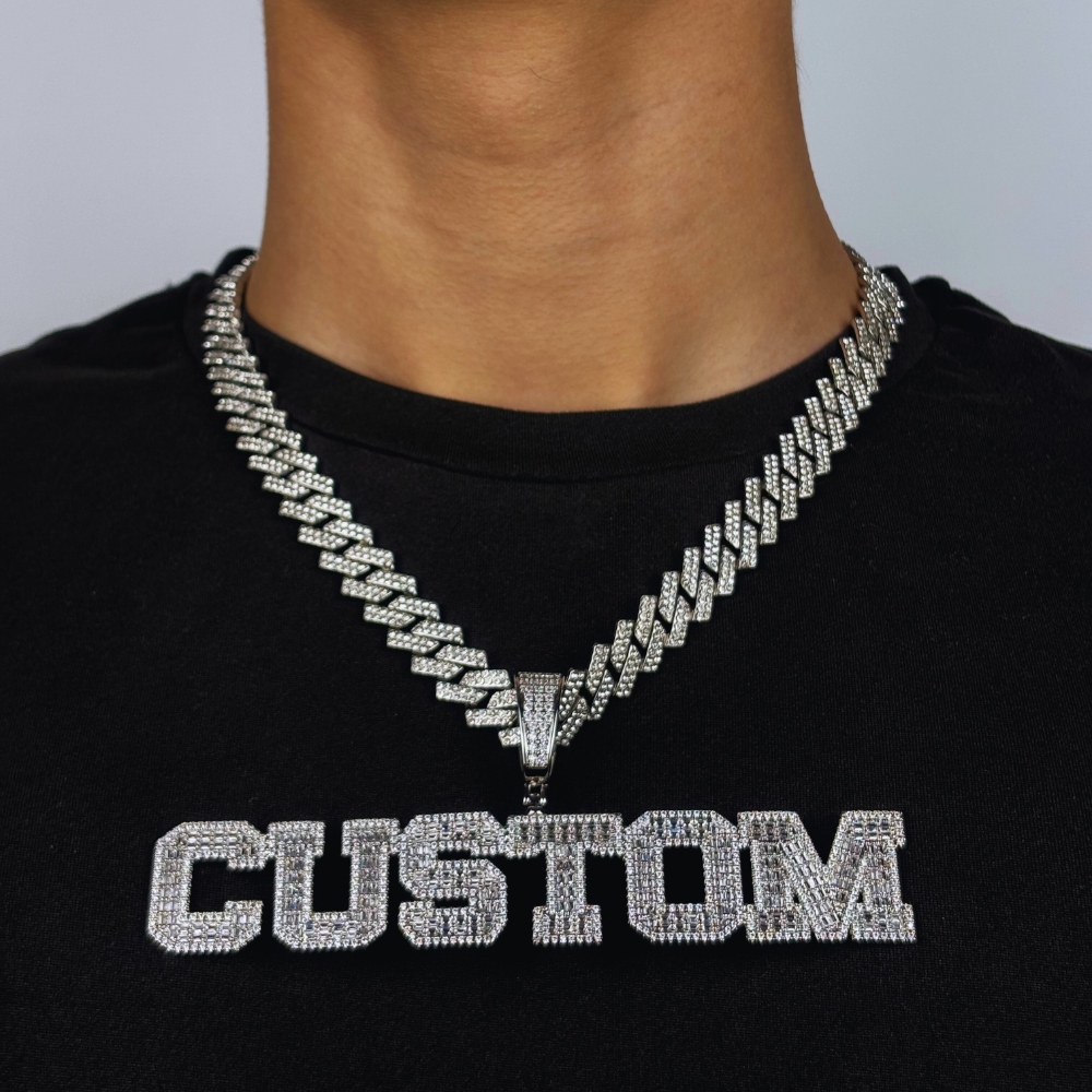 Modelo usa um pendente em forma de letra com design block, em ouro branco e totalmente cravejado com zircónias cúbicas, refletindo luxo personalizado e brilho refinado.