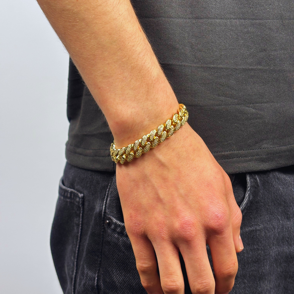 Modelo a exibir a pulseira 12mm Iced Miami Cuban Link em ouro, com um design imponente e luxuoso. Cada elo da pulseira é detalhadamente cravejado com pedras cintilantes, proporcionando um brilho deslumbrante. A peça combina sofisticação e estilo urbano, perfeita para adicionar um toque de glamour e ousadia ao seu visual.